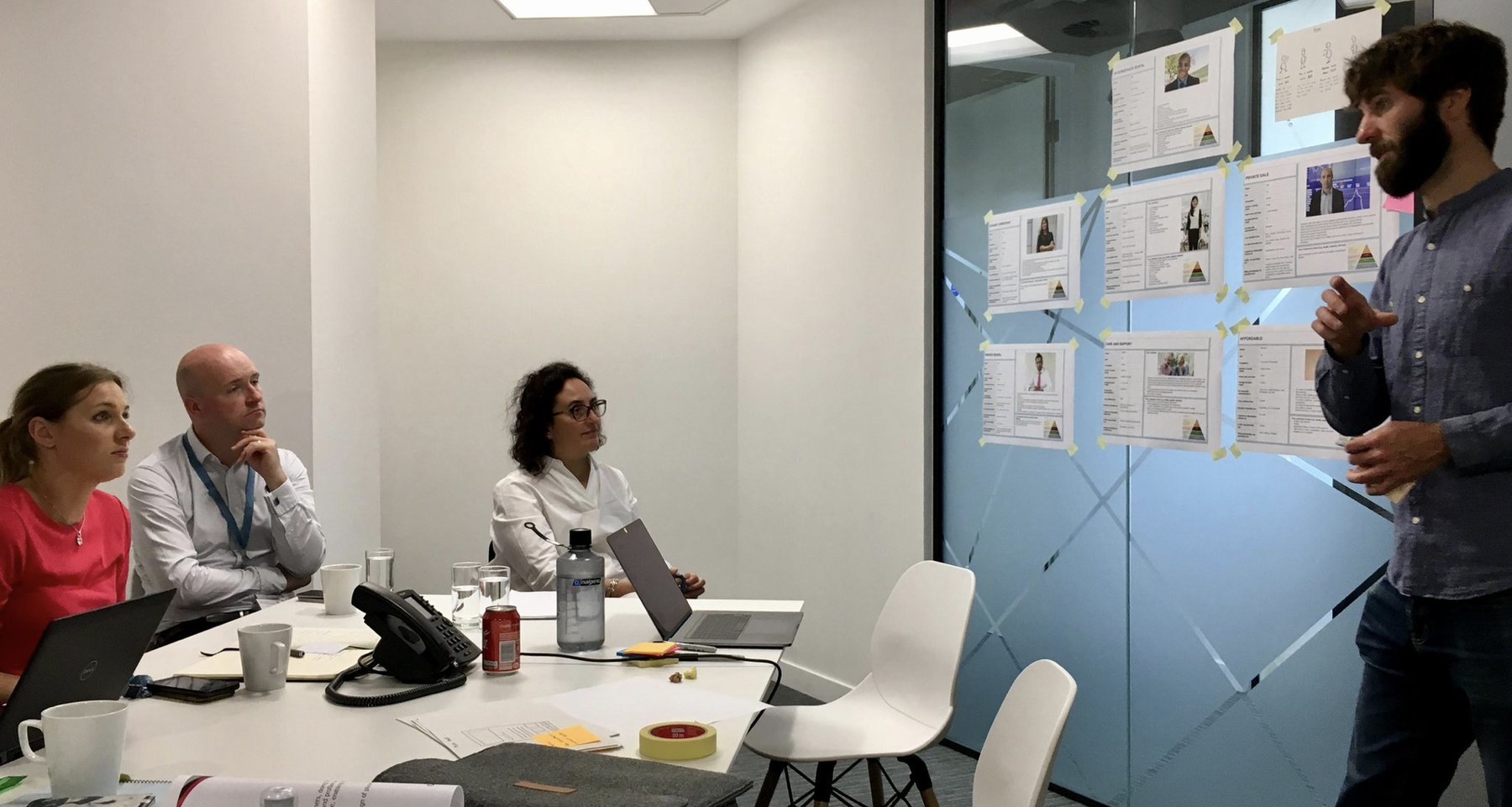Proto-personas taped to a glass wall while someone presents them to the group