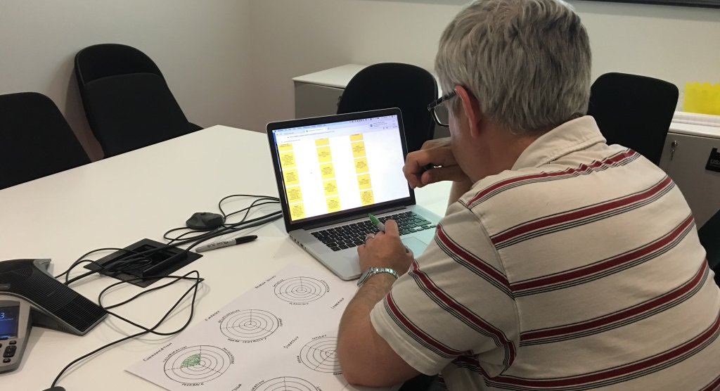 A designer working through the self-assessment on a laptop, printed skill diagrams on the desk